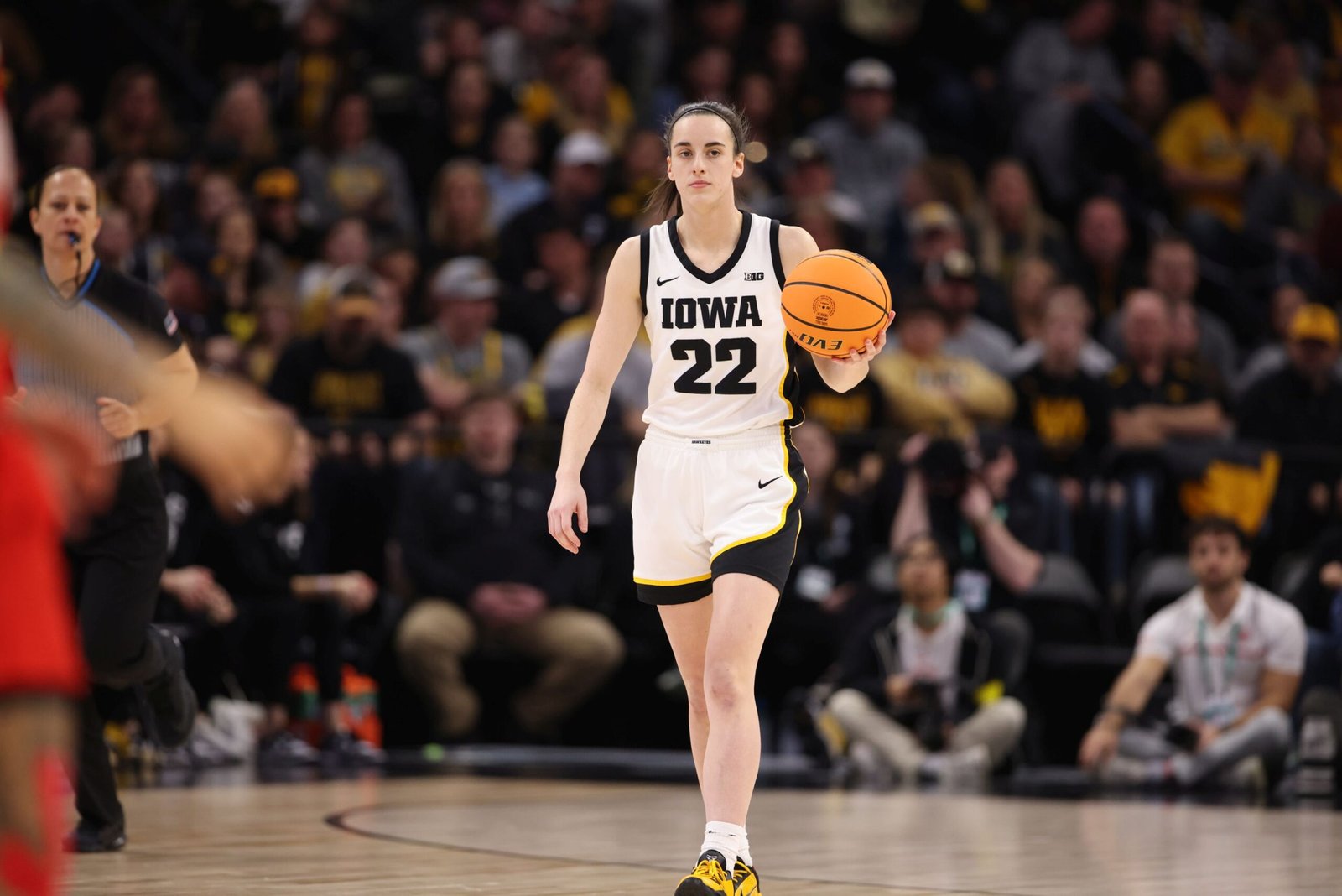 Caitlin Clark in a white Iowa jersey dribbles up the court during a game, featured in an article about Caitlin Clark net worth.