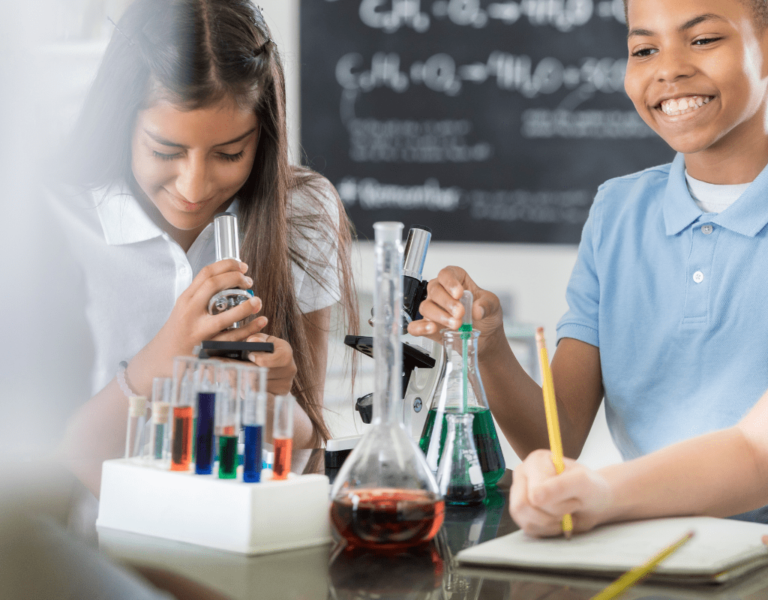 Students engaged in a science tutoring session, using microscopes, test tubes, and beakers while observing experiments and taking notes in a classroom setting.