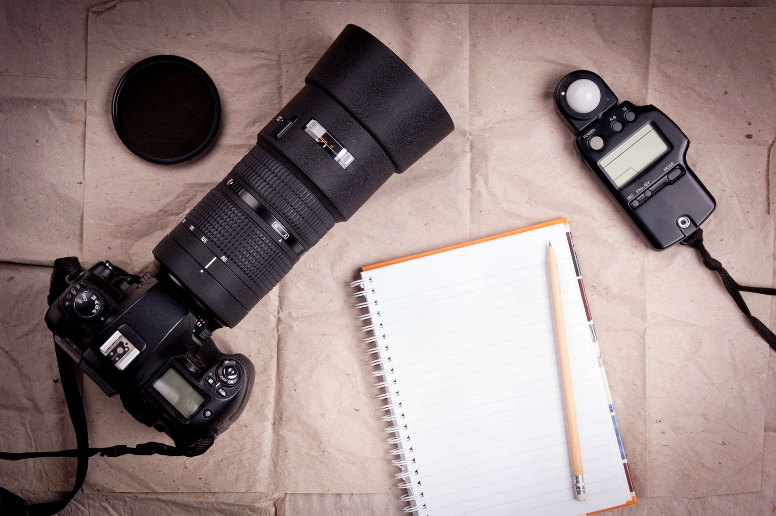 Photography workspace with camera, telephoto lens, light meter, and notebook for planning a photography business.