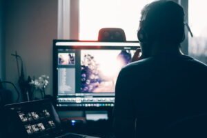 Person editing a photo on a computer in a dimly lit workspace with headphones on.