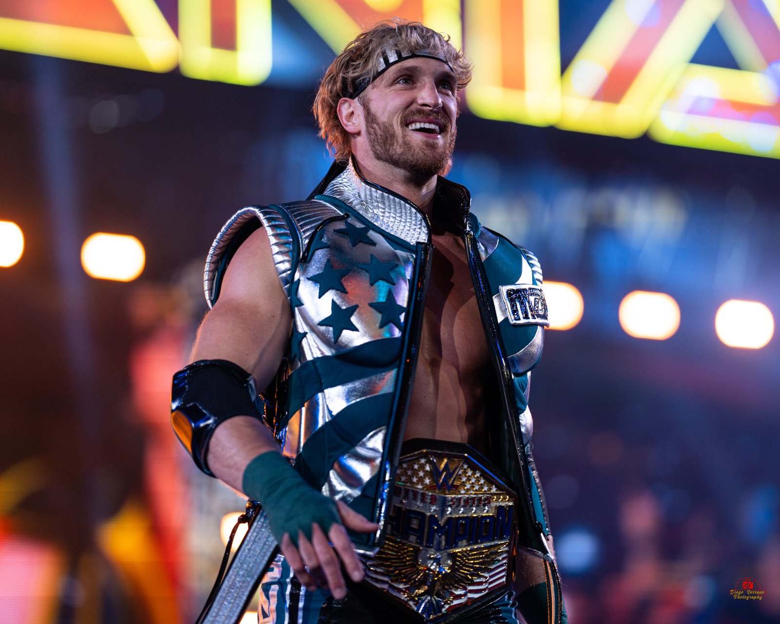 Logan Paul at Wrestlemania wearing metallic ring gear and a championship belt walks toward the stage lights during a live event, featured in an article about Logan Paul net worth.