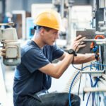 Industrial maintenance technician wearing a hard hat while inspecting and adjusting machinery.