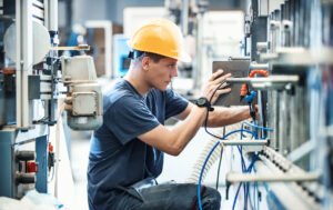 Industrial maintenance technician wearing a hard hat while inspecting and adjusting machinery.