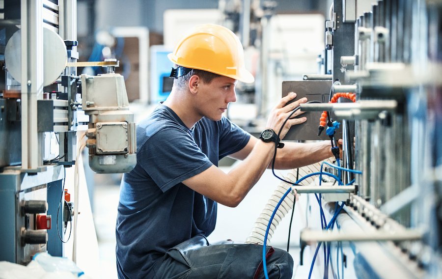 Industrial maintenance technician wearing a hard hat while inspecting and adjusting machinery.