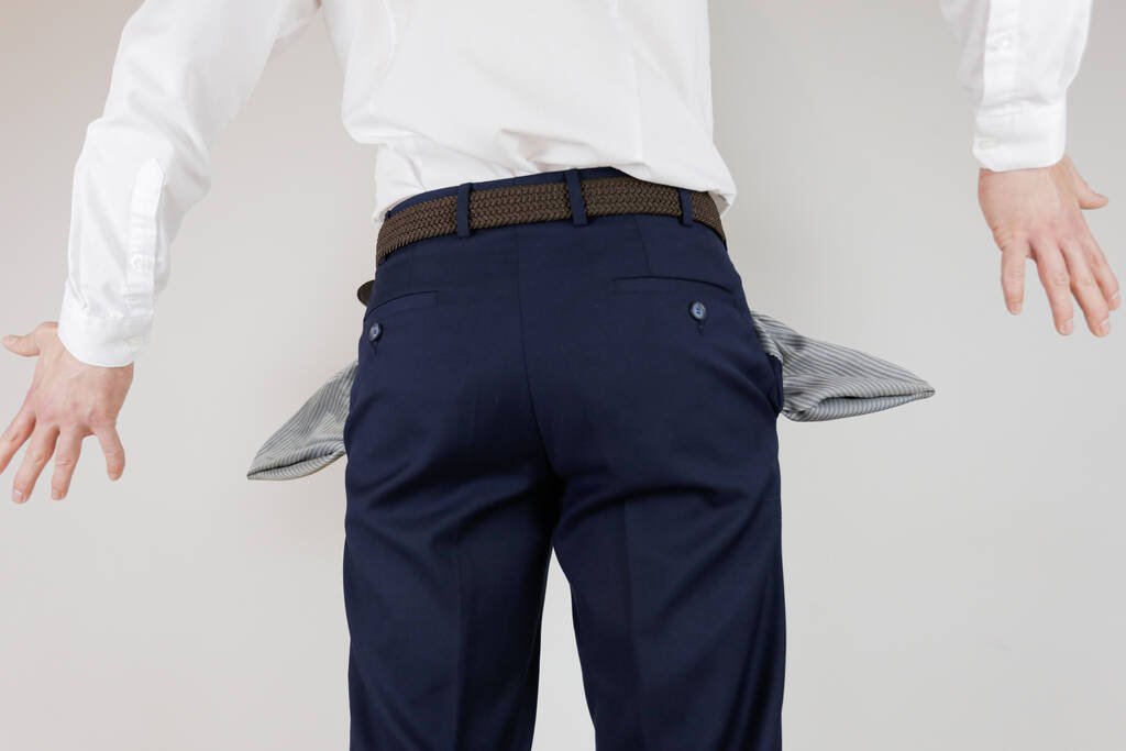 Businessman in a suit showing empty pockets to represent having no money or financial strain.